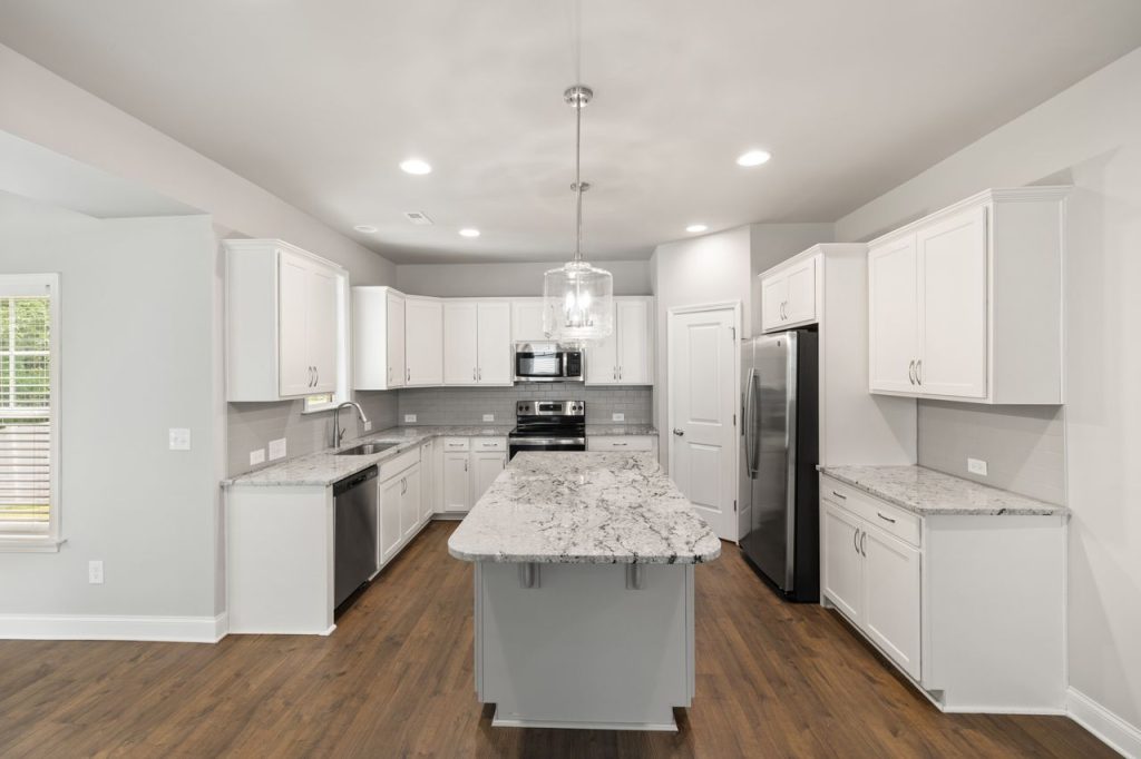 A spacious modern kitchen featuring white cabinets and a large granite island.
